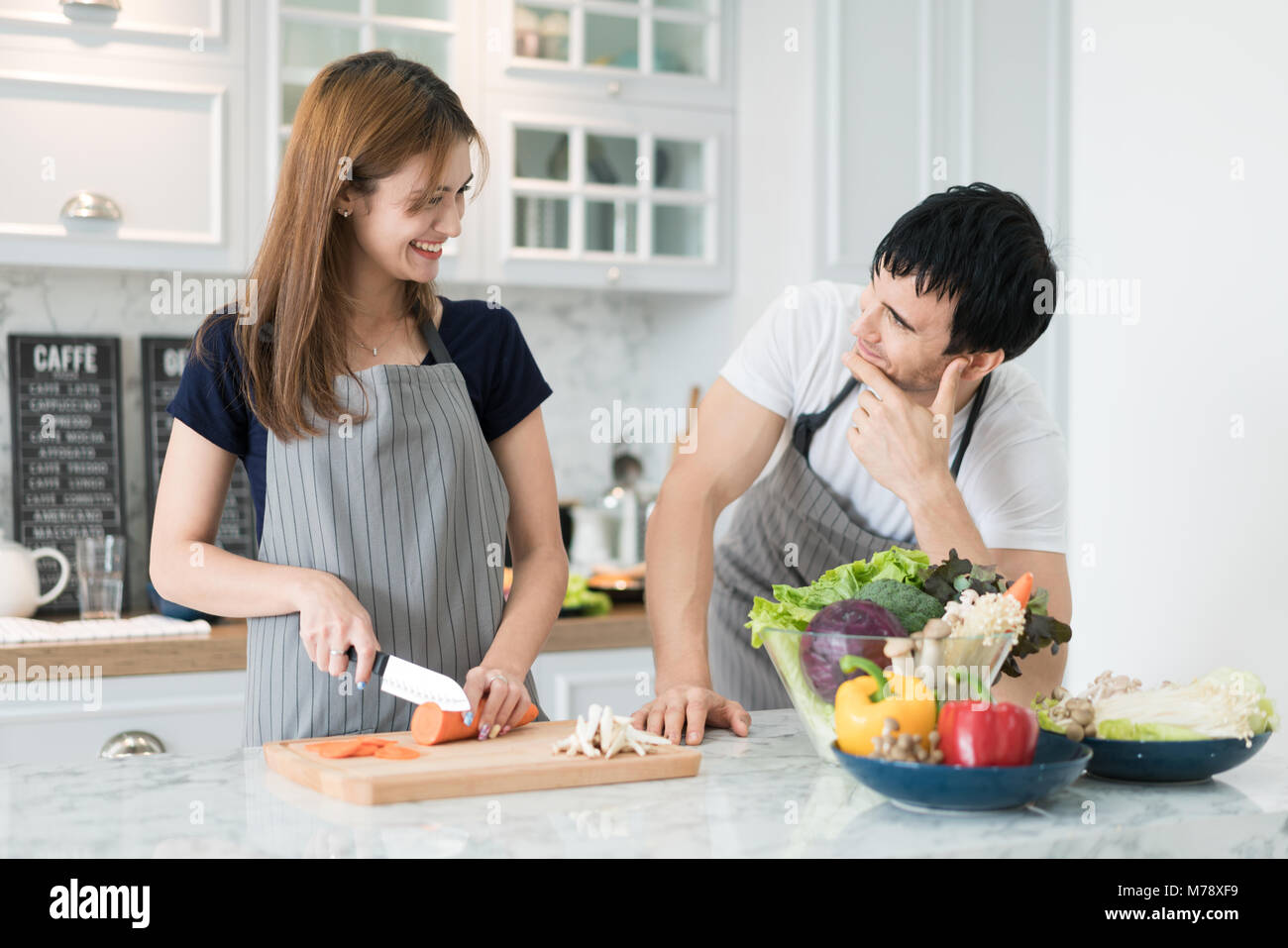 Young Asian couple preparing food together at counter in kitchen. Happy love couple concept. Stock Photo