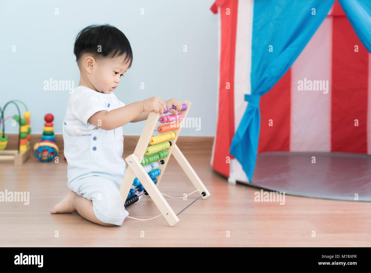 Asian baby boy learns to count. Cute child playing with abacus toy. Little boy having fun indoors at home. Educational concept for baby. Stock Photo