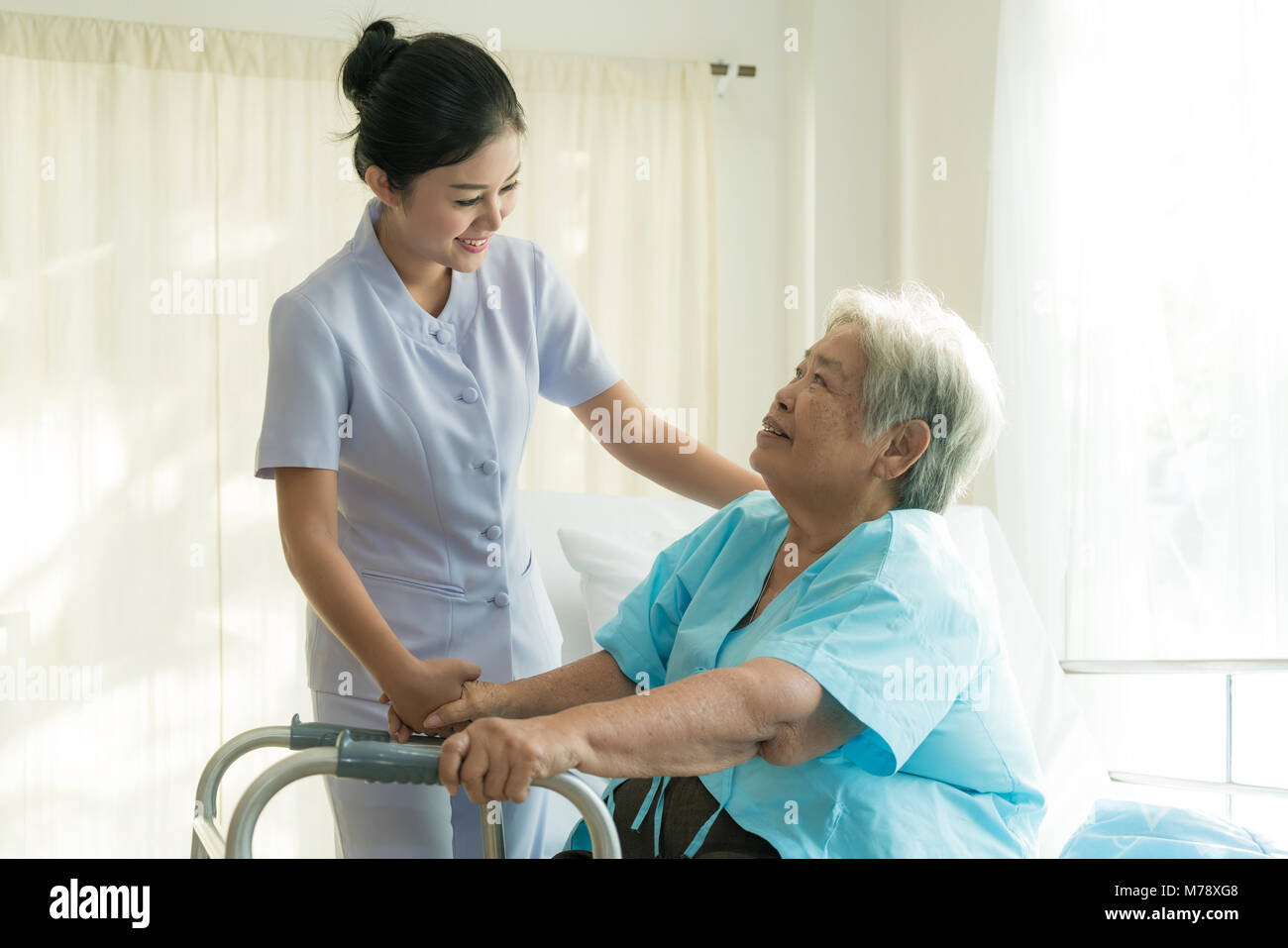 Asian young nurse supporting elderly patient disabled woman in using walker in hospital. Elderly patient care concept. Stock Photo