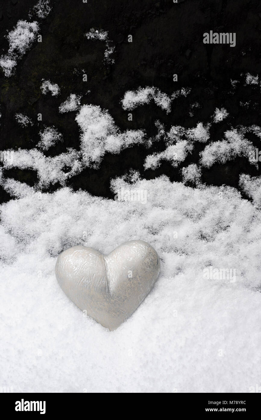 Silver grey painted heart placed against roofing slate upon which snow has settled. A landscape in minature mimicking snow falling through a dark sky Stock Photo