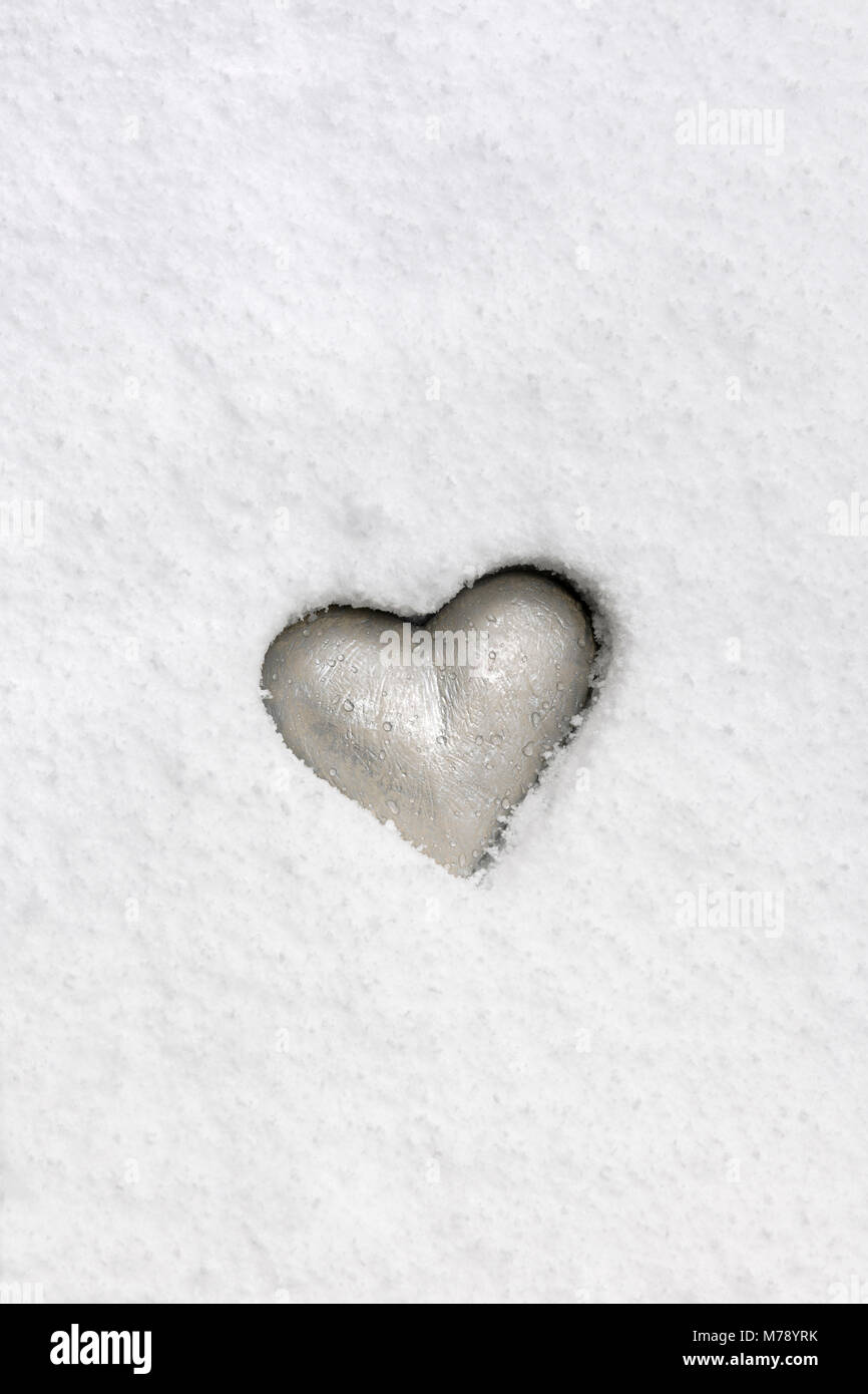 Silvery heart grey emedded in pristine snow. Stock Photo