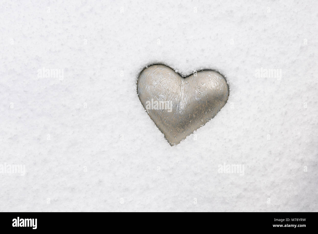 Silvery heart grey emedded in pristine snow. Stock Photo