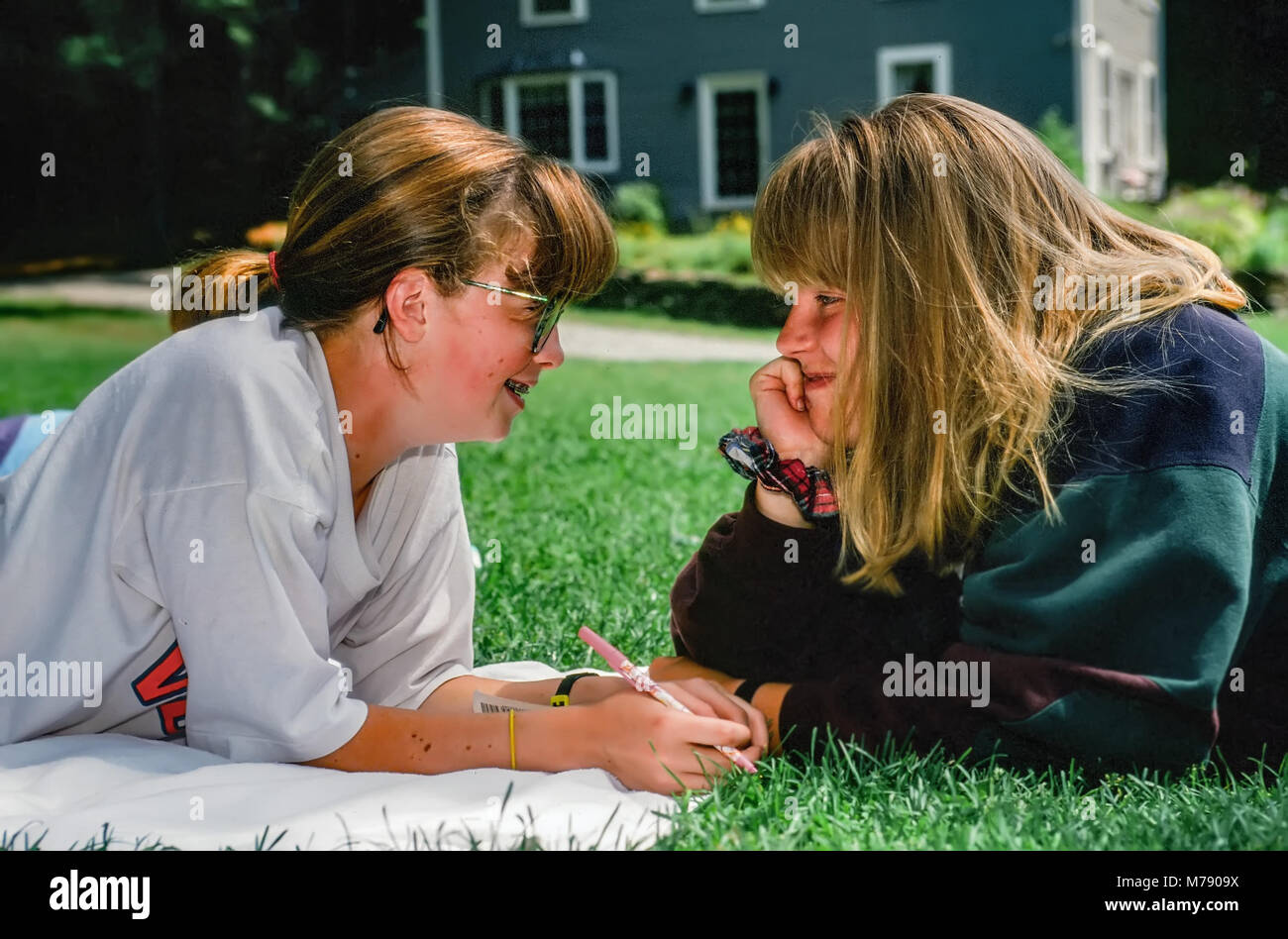 Two teenage girls lay on the grass face to face having a staring contest at summer camp in Vermont, USA. Stock Photo