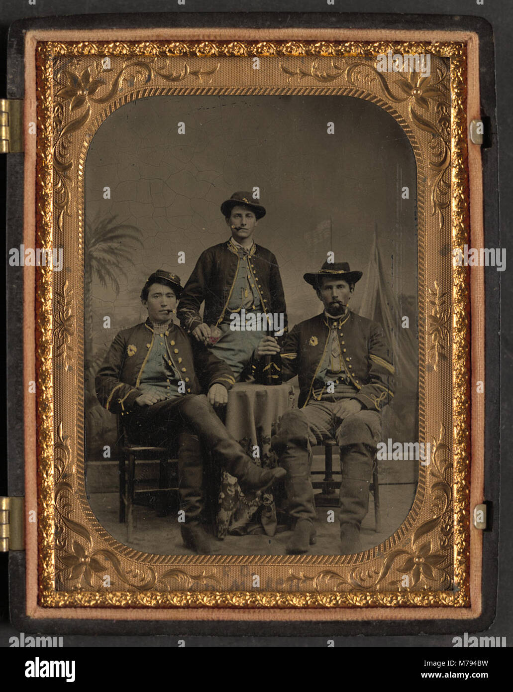 Three unidentified soldiers from the 75th New York Infantry Regiment who re-enlisted in Hancock's First Veterans Corps drinking wine and smoking cigars in front of painted backdrop showing LCCN2017645641 Stock Photo