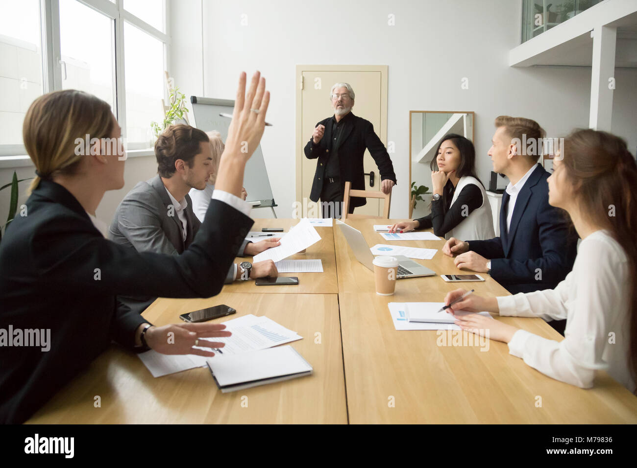 Businesswoman raising hand asking senior coach questions at team Stock Photo