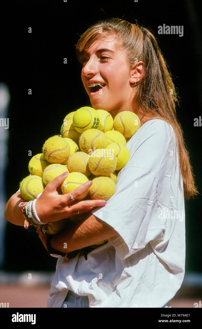 A teenage girl wearing teeth braces carries a large group of yellow tennis balls at summer camp in Vermont, United States, North America. Stock Photo