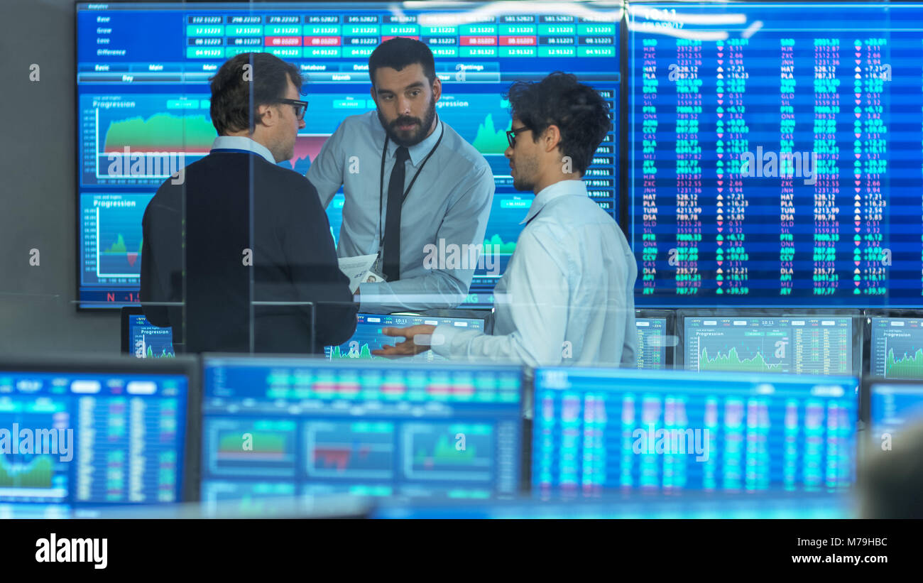 Three Experienced Stock Traders Talking Business. They Work for a Big Stock Exchange Firm. Office is Full of Displays Showing Data, Infographics Stock Photo