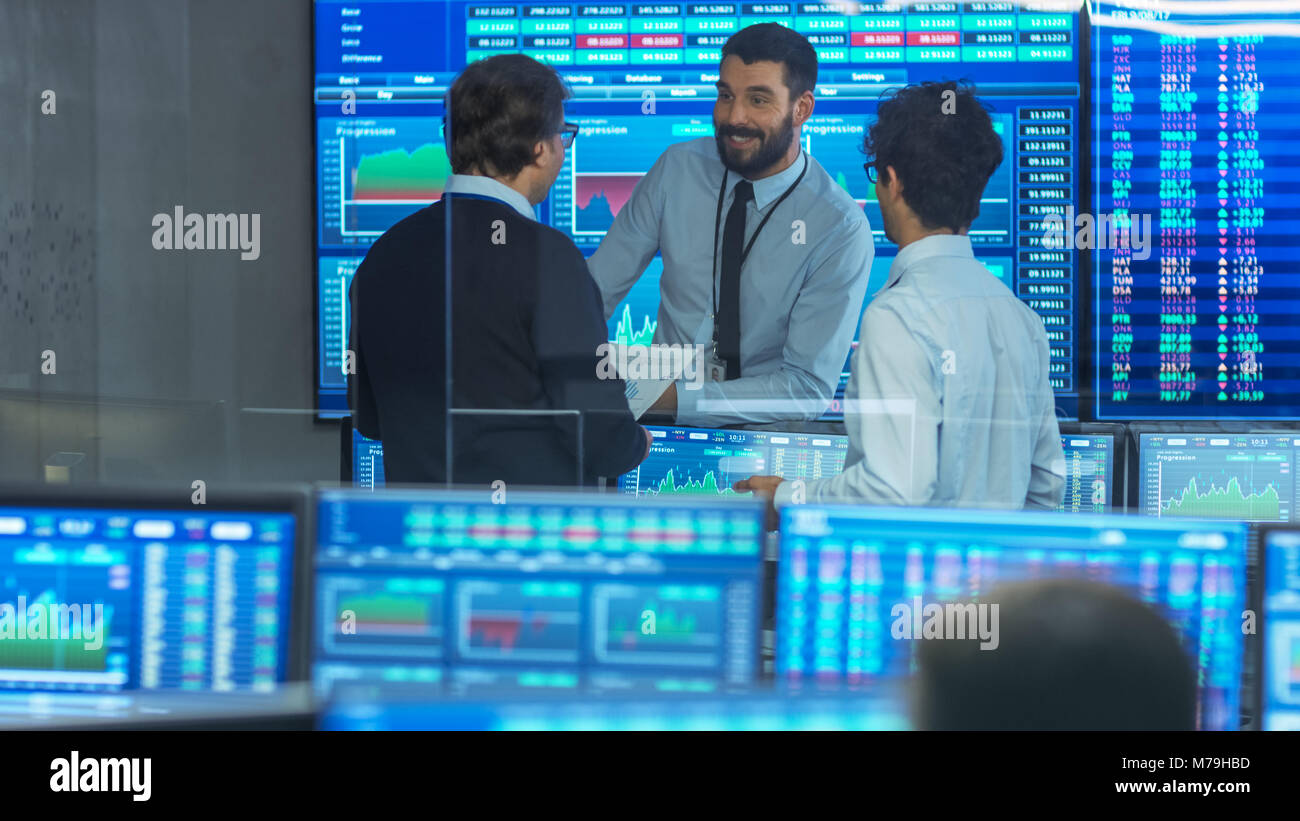 Three Experienced Stock Traders Talking Business. They Work for a Big Stock Exchange Firm. Office is Full of Displays Showing Data, Infographics Stock Photo