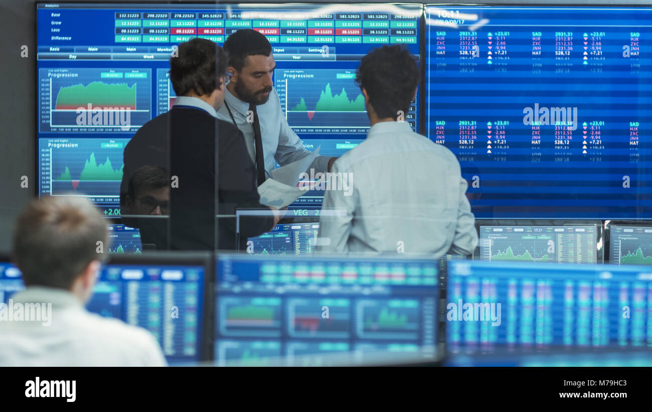 Three Experienced Stock Traders Talking Business. They Work for a Big Stock Exchange Firm. Office is Full of Displays Showing Data, Infographics. Stock Photo