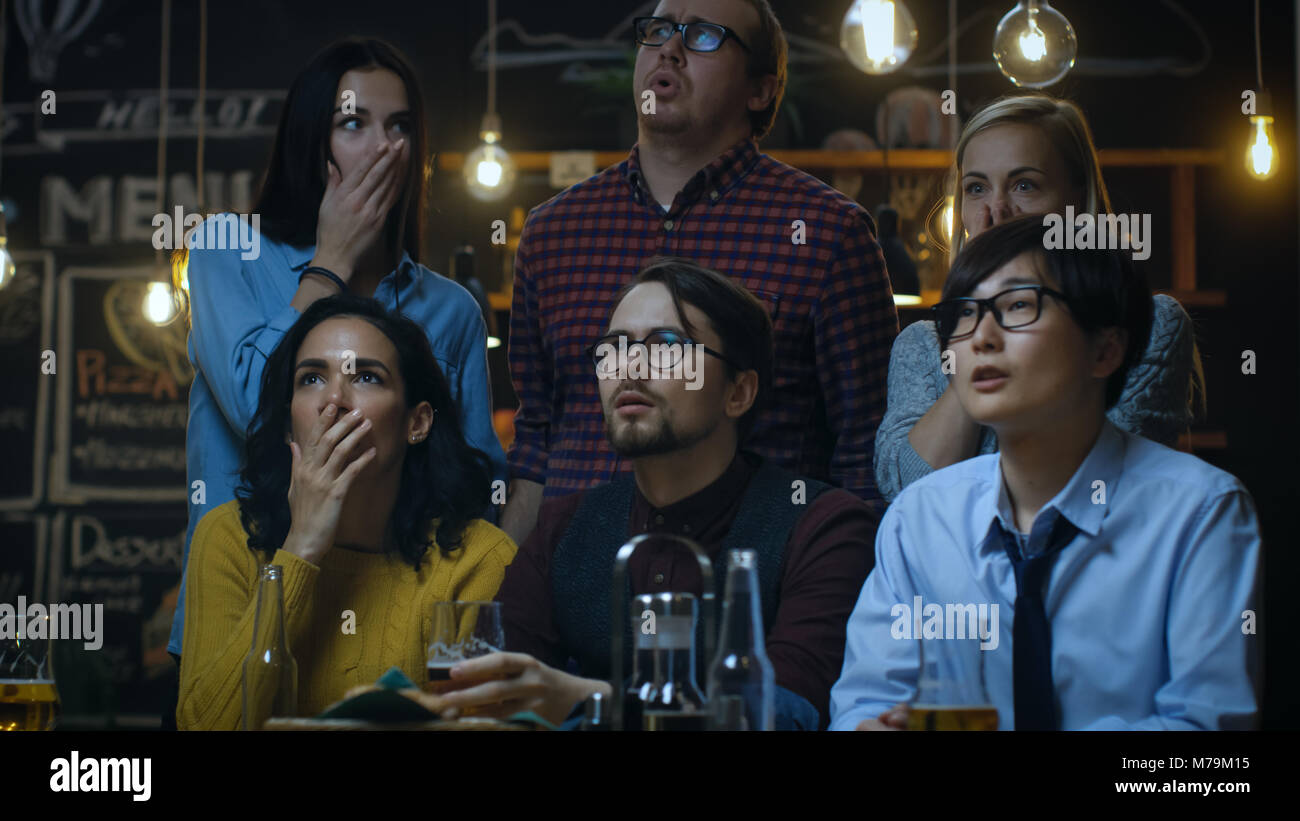 Young People in the Bar Watch TV Suddenly Breaking News Show that Tragic Events Unfold. Young People Are Horrified, Saddened and Shocked. Stock Photo