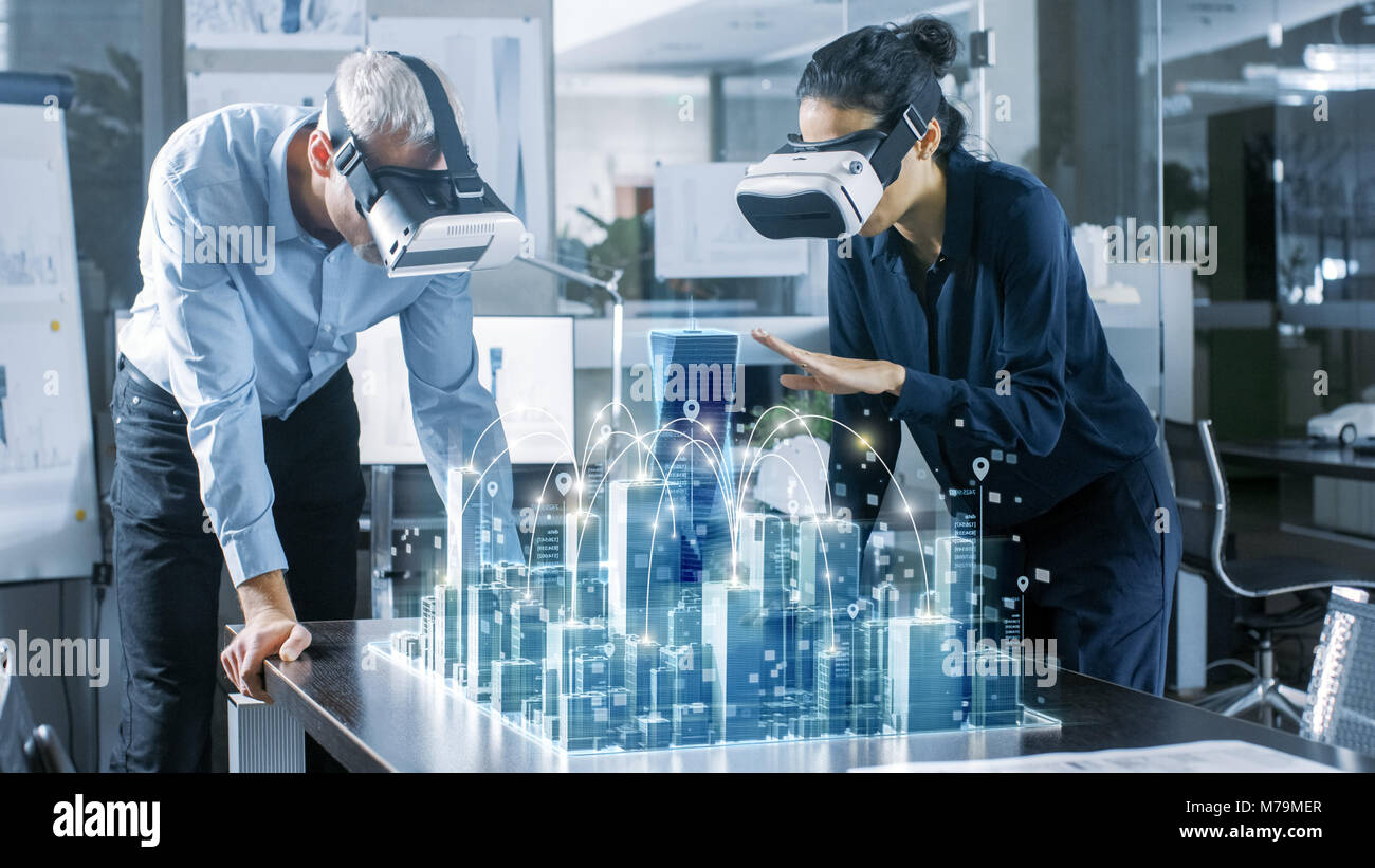 Male and Female Architects Wearing  Augmented Reality Headsets Work with 3D City Model. High Tech Office Professional People Use Virtual Reality Model Stock Photo