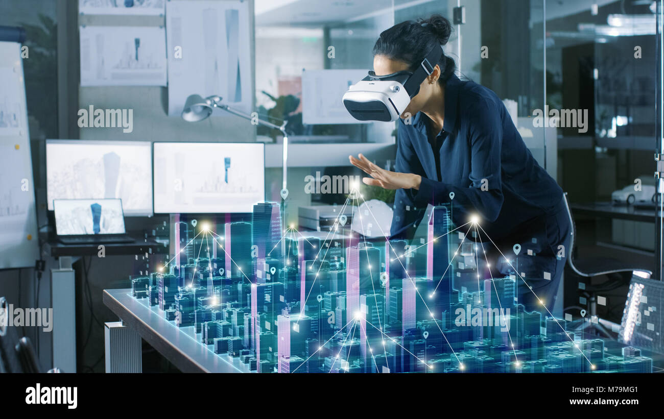 Professional Female Architect Wearing Makes Gestures with Augmented Reality Headset Shows Statistics for 3D City Model. High Tech Office Use VR Helmet Stock Photo