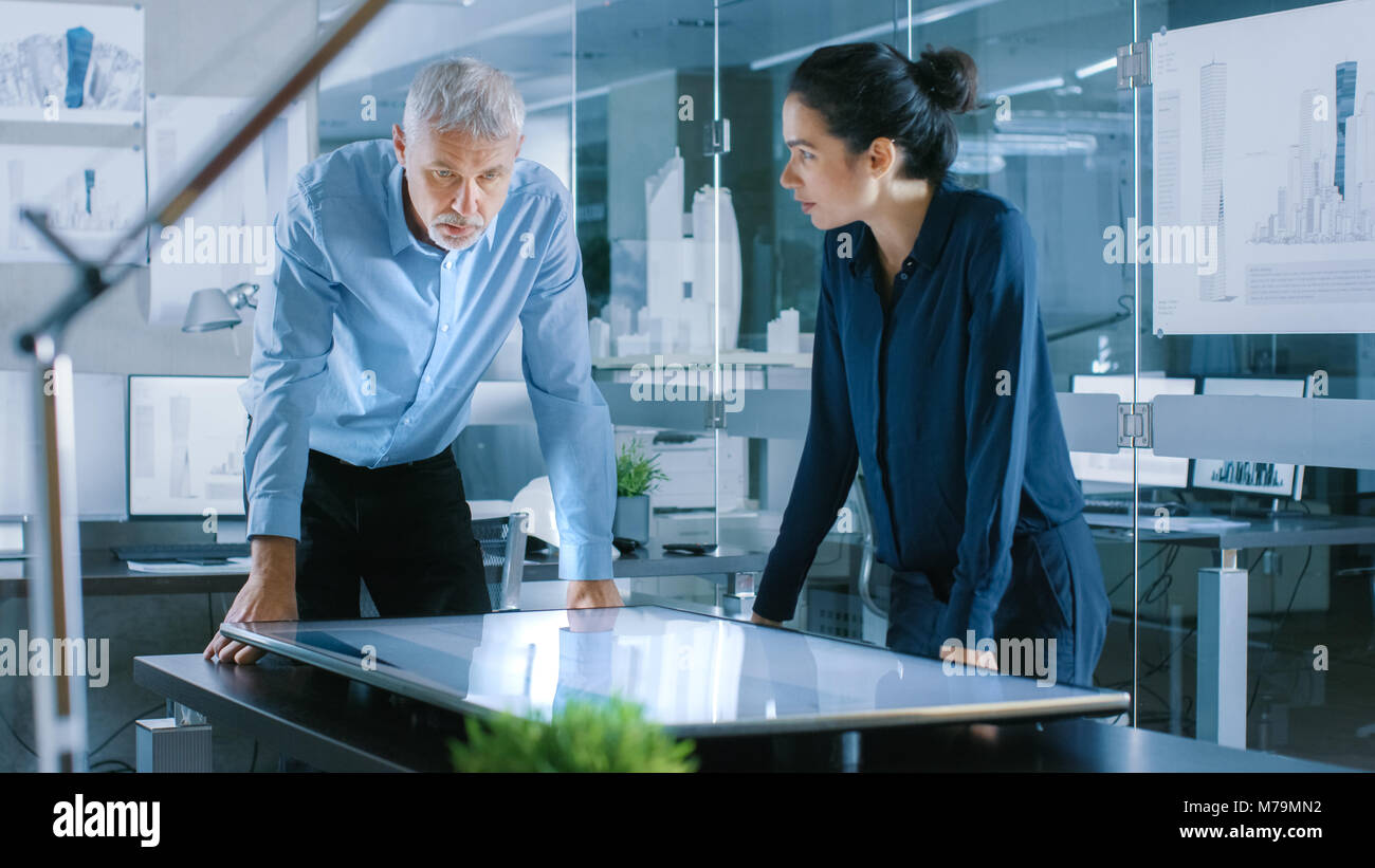 Senior Male and Young Female Architectural Designers Draw Building Concept on a Graphics Tablet Display Vertical Touchscreen Table. Stock Photo