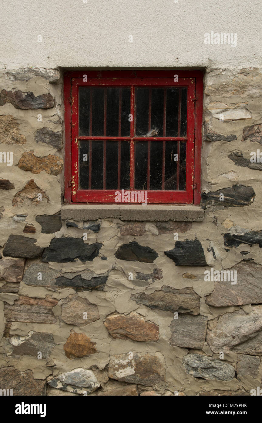 Square red wooden window in a stone and whitewashed wall of an outbuilding or house Stock Photo
