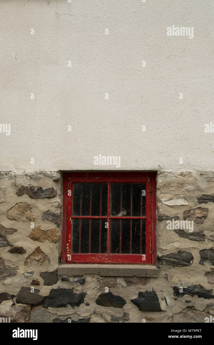 Square red wooden window in a stone and whitewashed wall of an outbuilding or house, whitespace Stock Photo