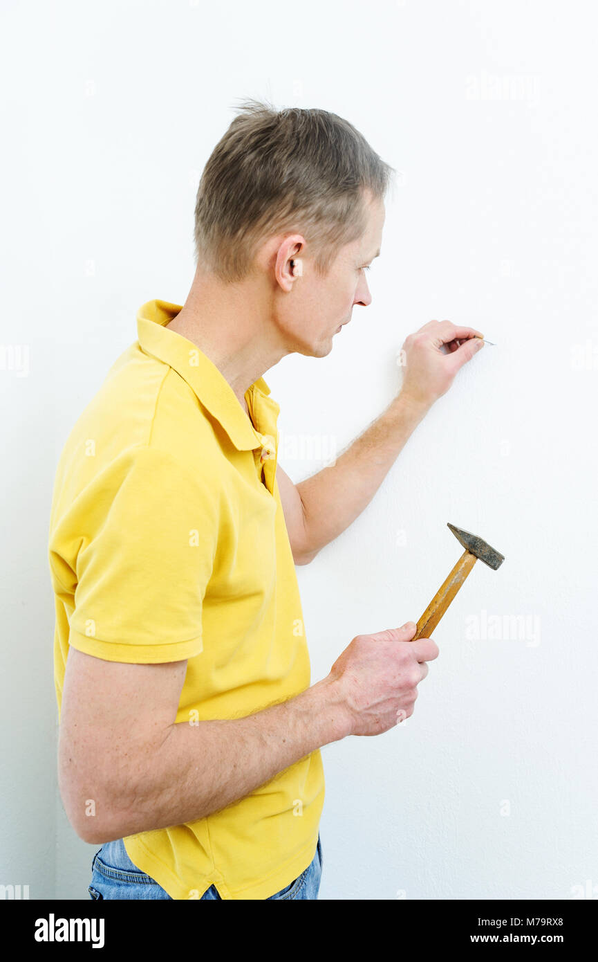 The man is putting a nail into the wall to hang a picture. Stock Photo