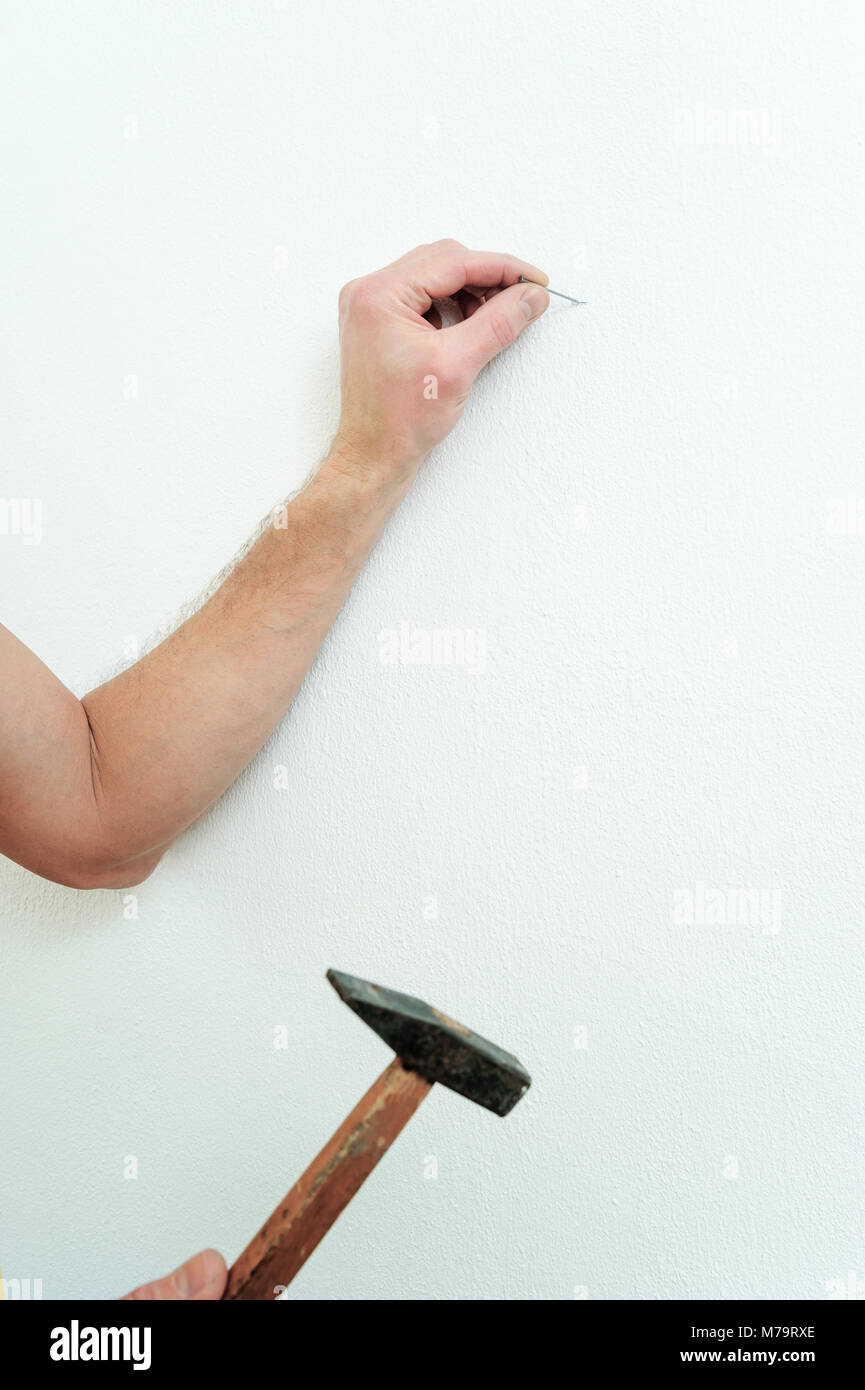 Man's hand is putting a nail into the wall to hang a picture. Stock Photo