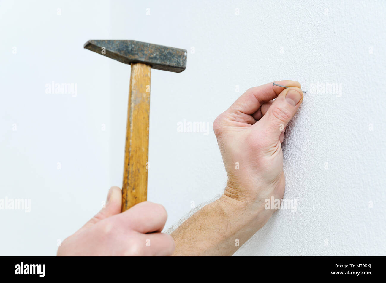 Man's hand is putting a nail into the wall to hang a picture. Stock Photo