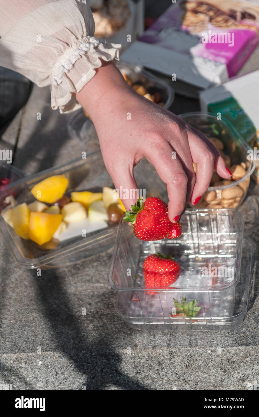 woman's hand picks up a strawberry from a plastic box Stock Photo