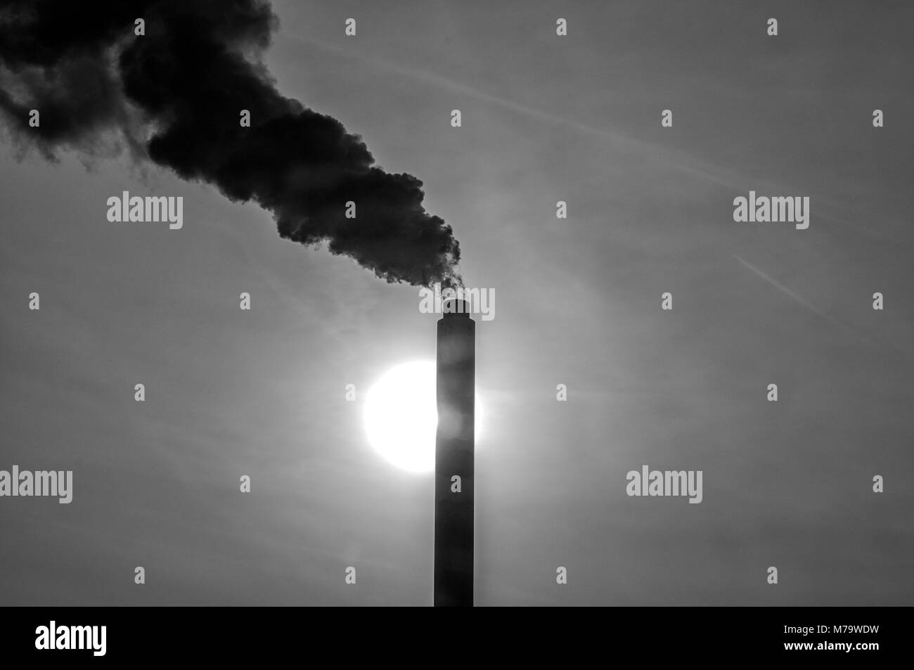 silhouette of a high industrial pipe with the sun behind it Stock Photo