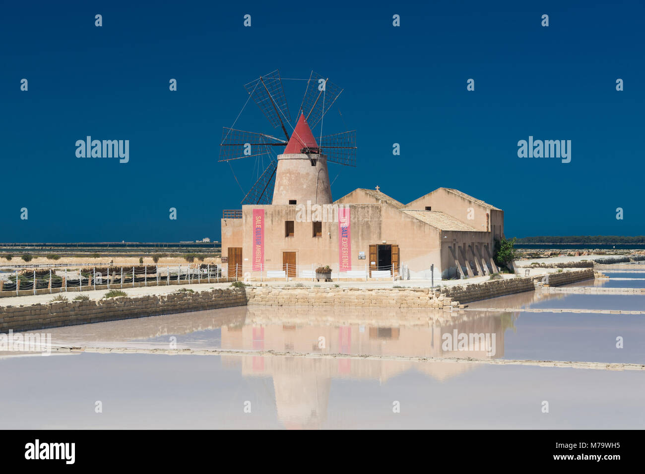 The salt museum with a windmill with reflection in the salt pans at the salina of Mozia at the west coast of Sicily between Trapani and Marsala. Stock Photo