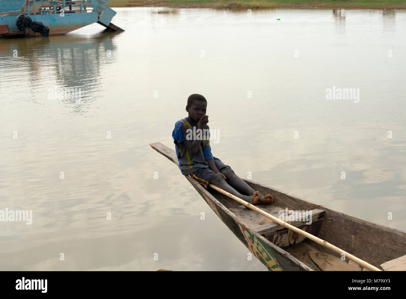 A young local boy sitting at the stern of a pirogue (traditional boat) on the River Bani. Mopti Region, Mali, West Africa. Stock Photo