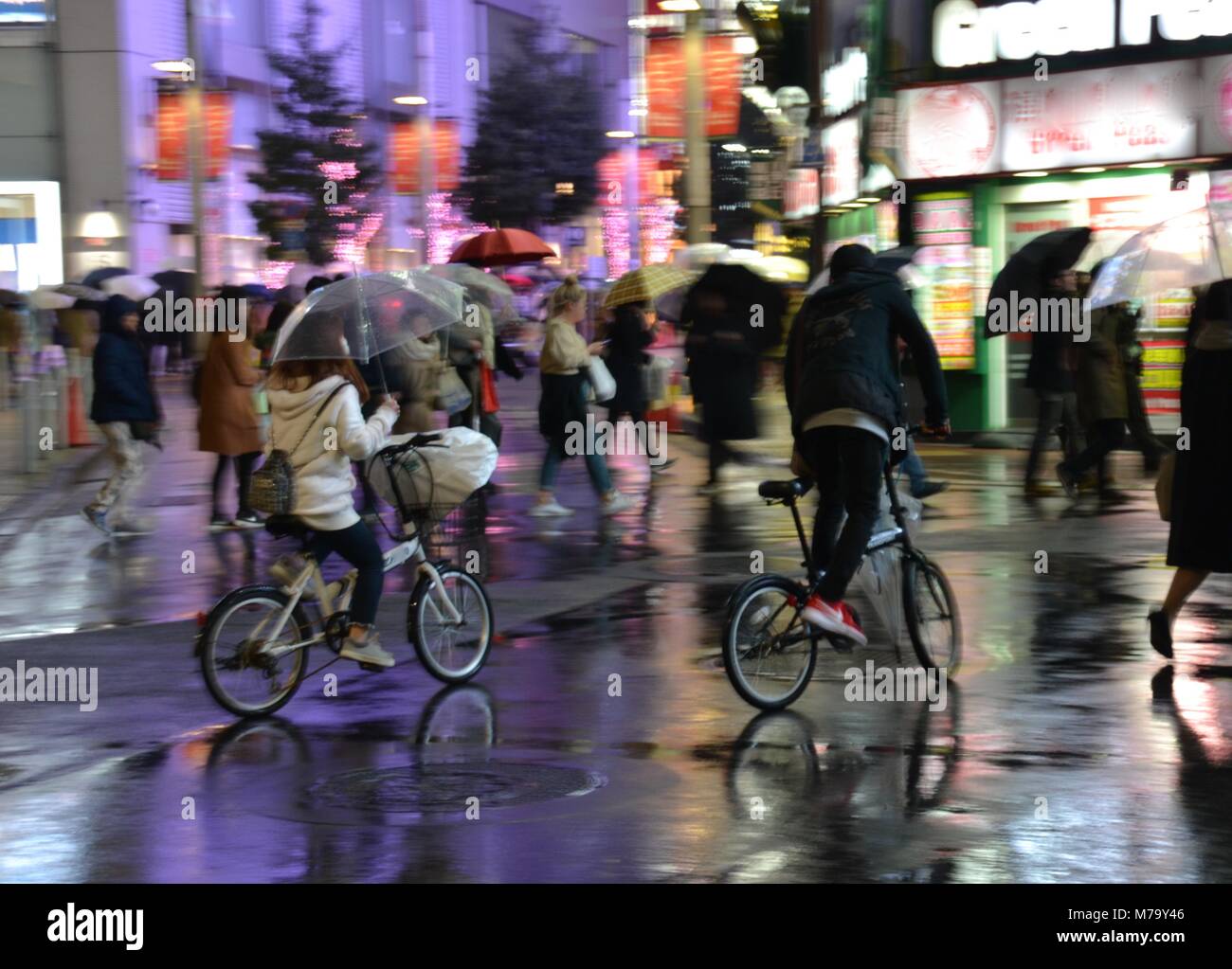 BMX bicycles riding through Tokyo on a raining night with bright neon lights Stock Photo