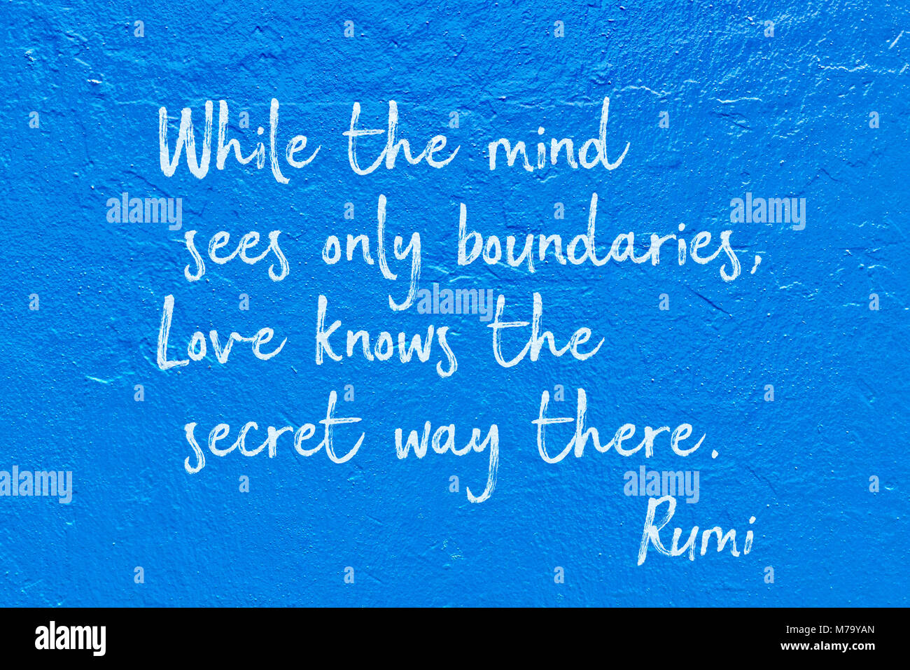 While the mind sees only boundaries, Love knows the secret way there - ancient Persian poet and philosopher Rumi quote handwritten on blue wall Stock Photo