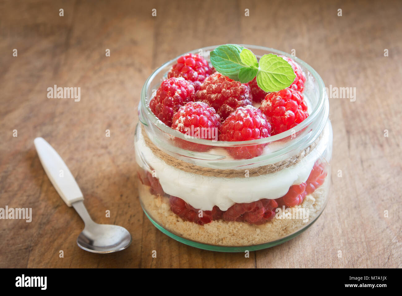 Raspberry cheesecake in glass jar with fresh raspberries and cream cheese  on wooden background. Healthy homemade summer berry layered dessert. Stock Photo