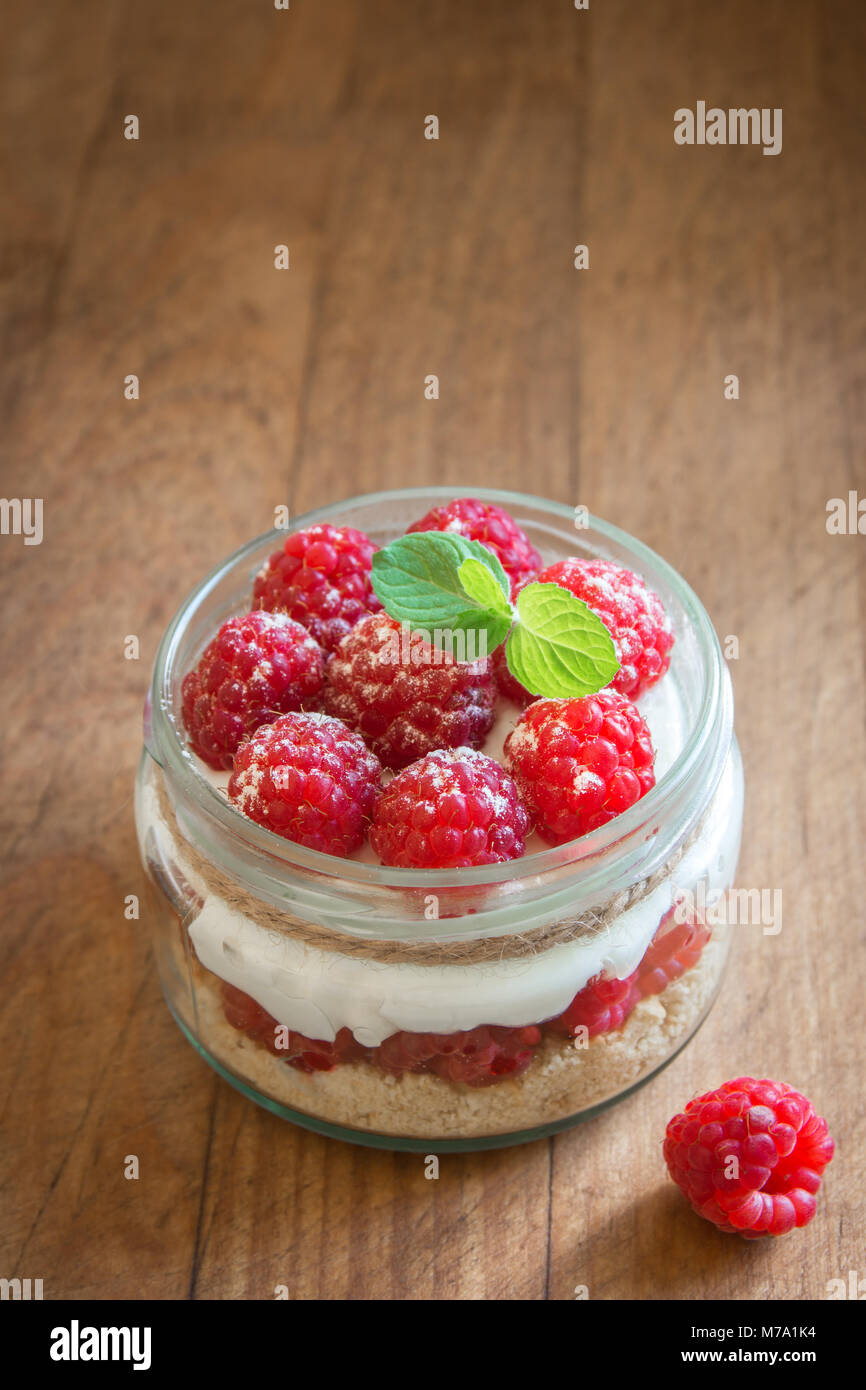Raspberry cheesecake in glass jar with fresh raspberries and cream cheese  on wooden background. Healthy homemade summer berry layered dessert. Stock Photo