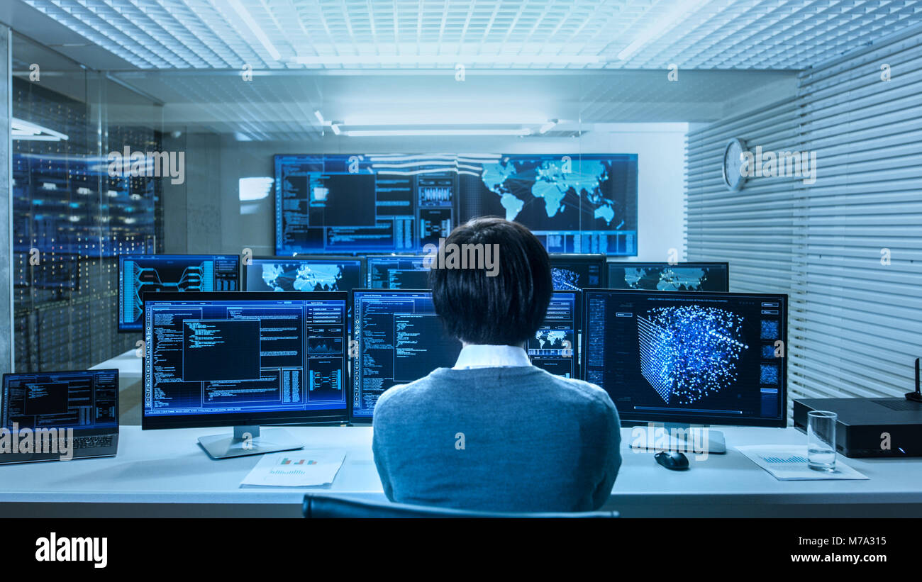 In the System Control Data Center Technician Operates Multiple Screens with Neural Network and Data Mining Activities. Room is Full of Monitors Stock Photo