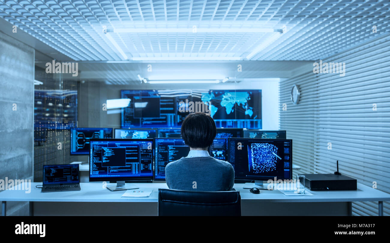 Back View of the IT Engineer Working with Multiple Monitors Showing Graphics, Functional Neural Network. He Works in a Technologically Advanced System Stock Photo