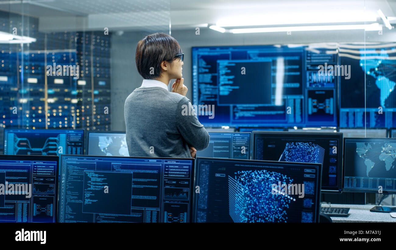 In the System Control Room Technical Operator Stands and Monitors Various Activities Showing on Multiple Displays with Graphics. Administrator Monitor Stock Photo