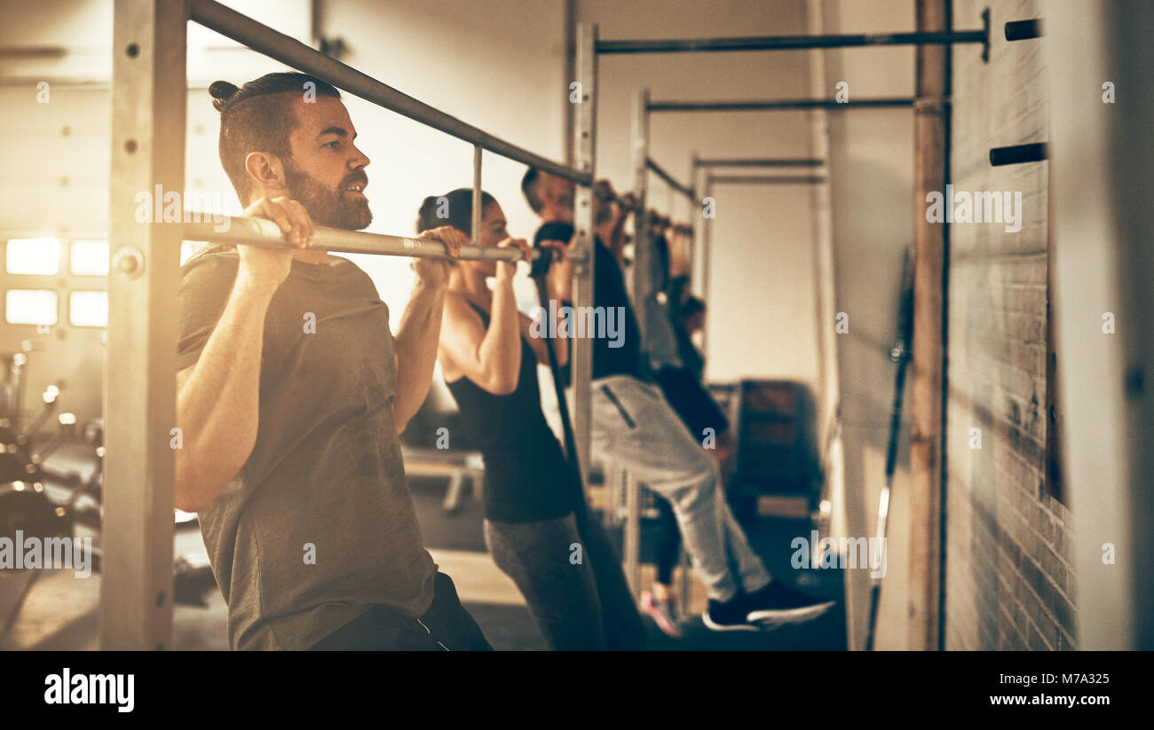 Group of fit people in sportswear doing chin ups while working out together at the gym Stock Photo