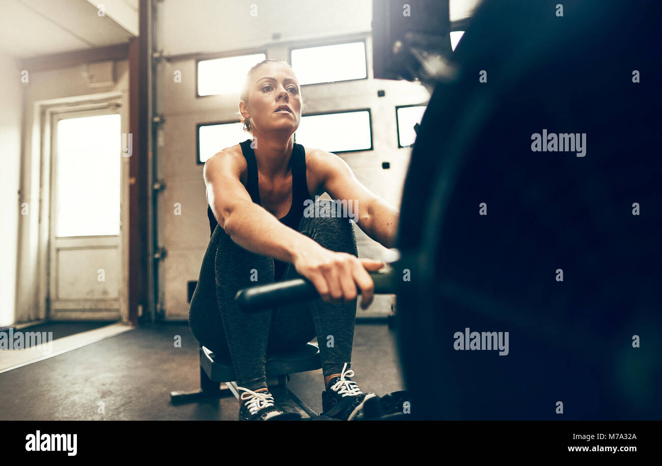 Fit young woman in sportswear exercising on a rowing machine during a ...