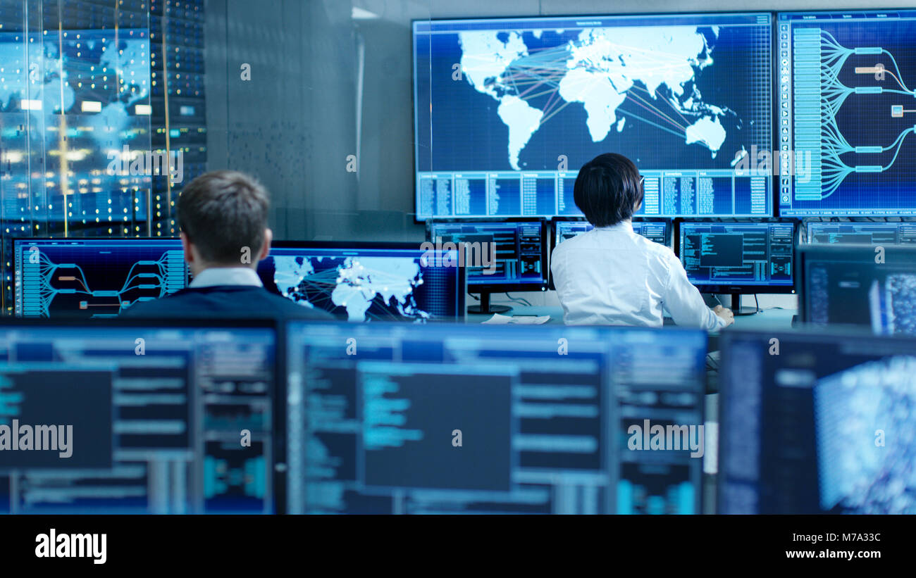 In the System Control Room Operator and Administrator Sitting at Their Workstations with Multiple Displays Showing Graphics and Logistics Information. Stock Photo