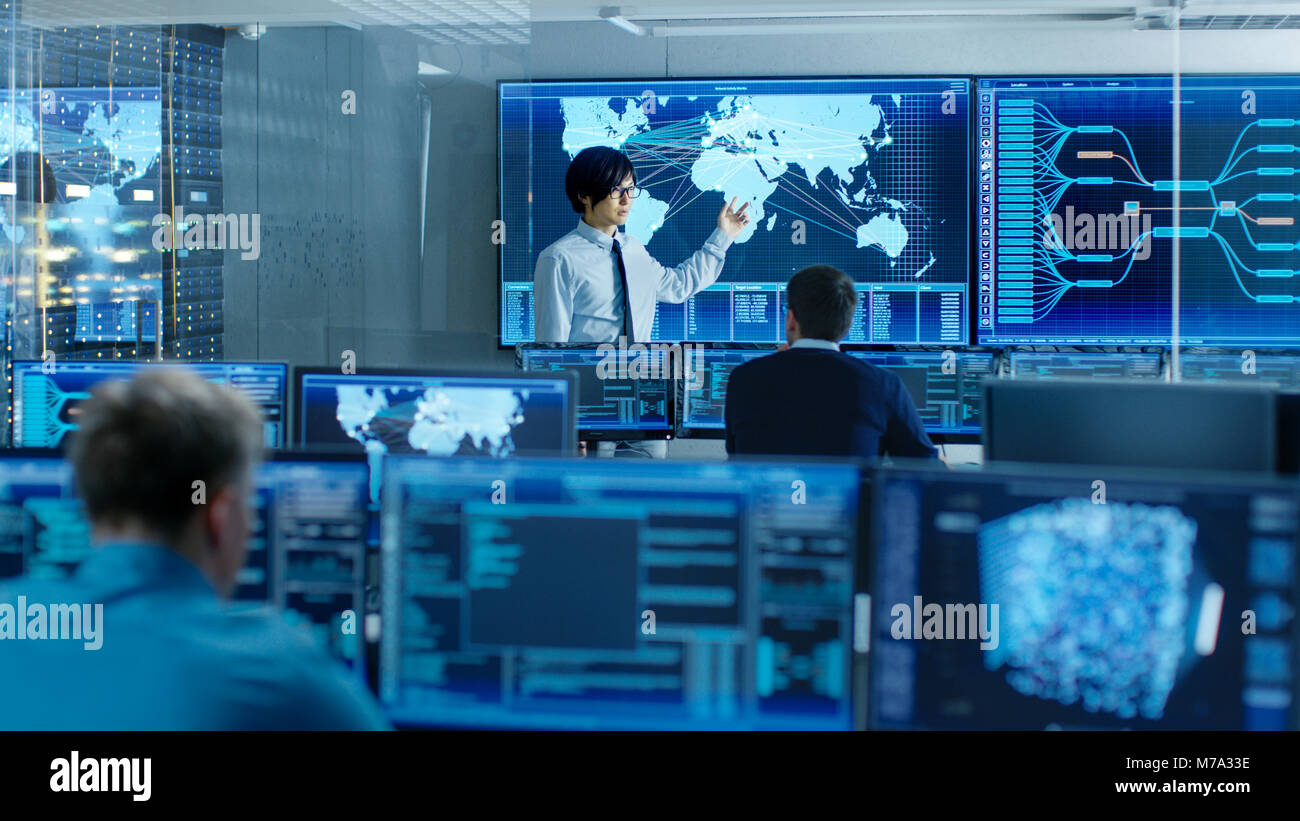 In the System Control Room Manager Holds a Briefing for His Staff Members. They're Work in Data Center and are Surrounded by Multiple Screens Stock Photo