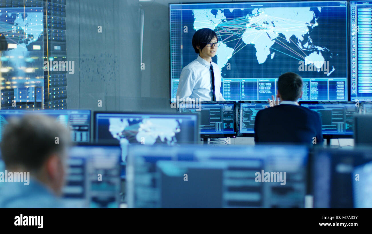 In the System Control Room Manager Holds a Briefing for His Staff Members. They're Work in Data Center and are Surrounded by Multiple Screens Stock Photo