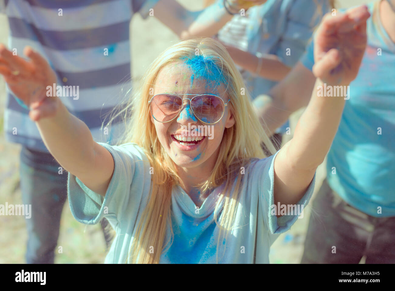 High Angle Shot of Blonde Girl Throwing Colorful Powder in the Crowd Amidst Hindu Holi Festival Celebrations. They Have Enormous Fun on this Sunny Day Stock Photo