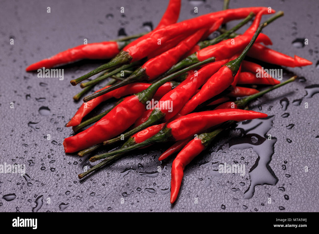 A close up photo of wet spicy red peppers on a black background Stock
