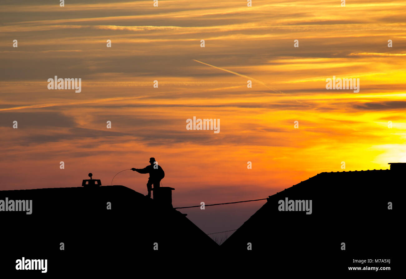 Chimney sweep at work on the rooftop - sunset and silhouette Stock Photo