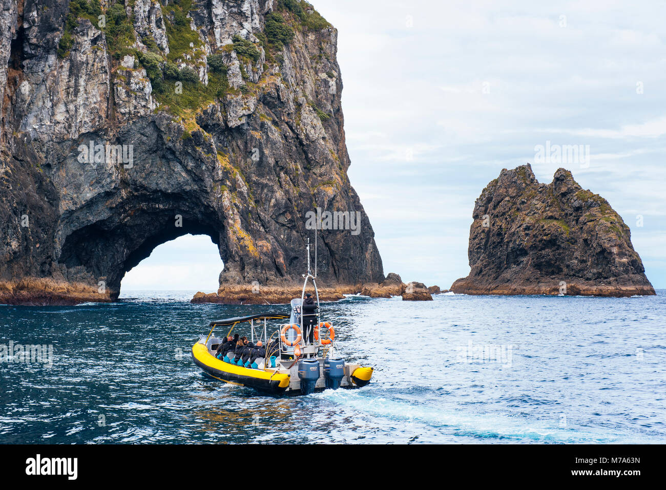 Tourist boat approaching the Hole in the Rock on Piercy (Motukokako) Island just off Cape Brett in the Bay of Islands area, North Island, New Zealand Stock Photo