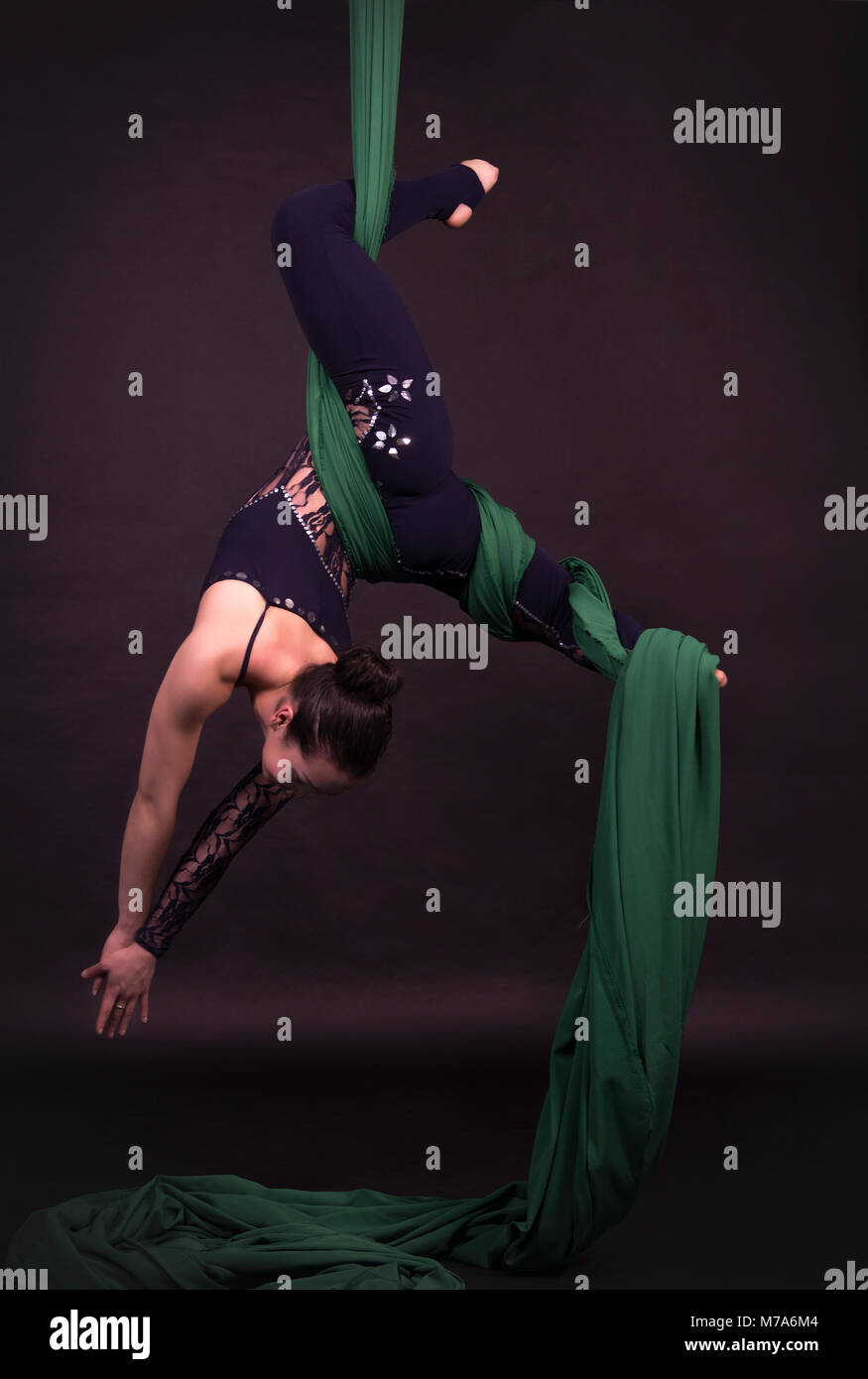 Young, smiling woman does exercises on the canvases. Studio recording of the performance on a dark background. Stock Photo