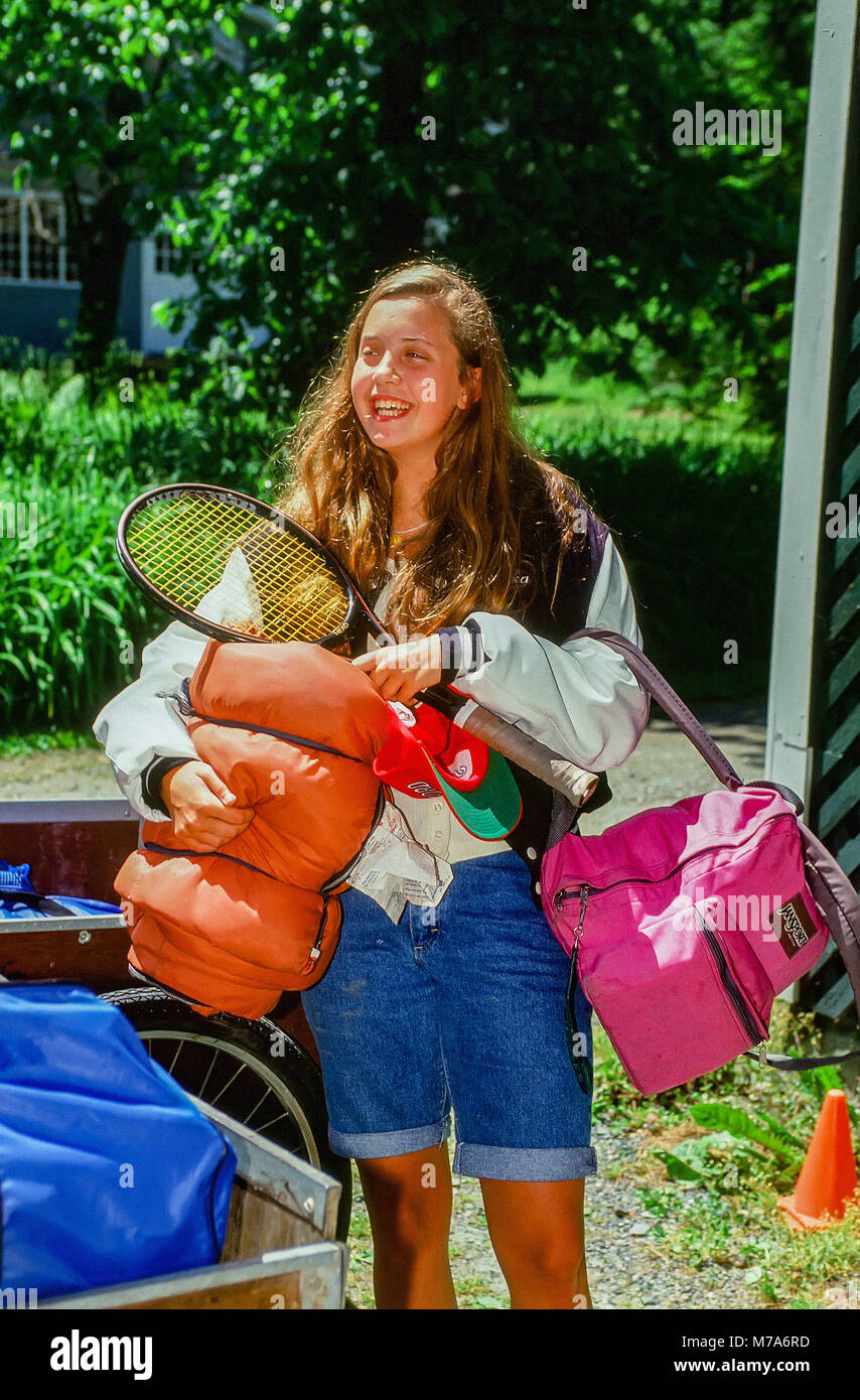 A 18-year old girl arrives at summer camp with her tennis racket, sleeping bag and backpack to start her job as a counselor at a girls' summer camp in Stock Photo