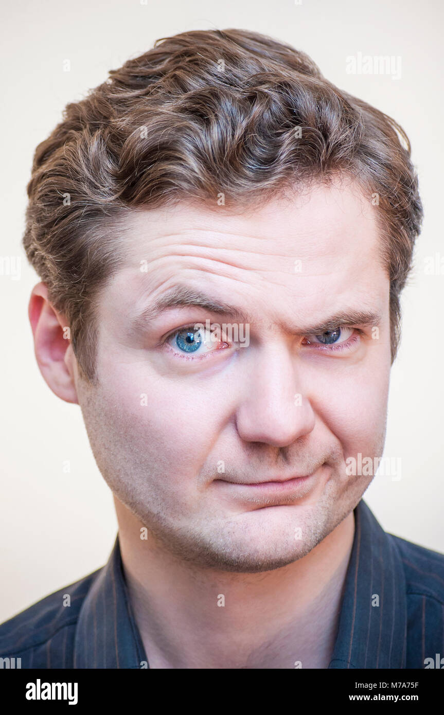 Portrait of young man questionably mistrustfully looking with raised eyebrow on white background. Stock Photo