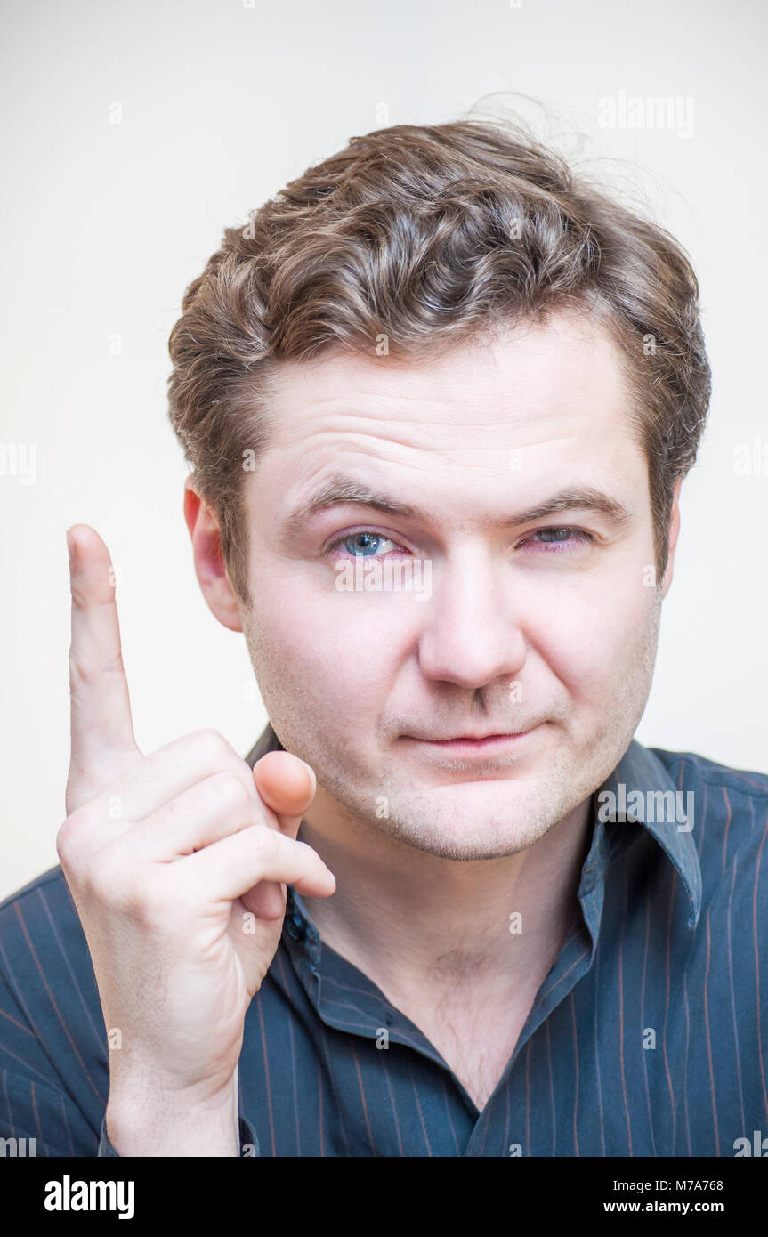 Portrait of young cunning tricky blue-eyed man got great idea and pointing with finger up on white background. Stock Photo