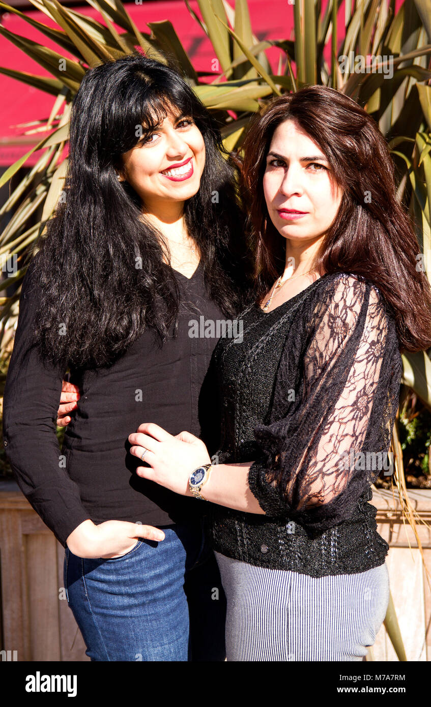 Two female University students, Parisian-Algerian Faiza Faa (left) and friend Samar Munaf from Iraq (right) standing hugging each other in Dundee, UK Stock Photo