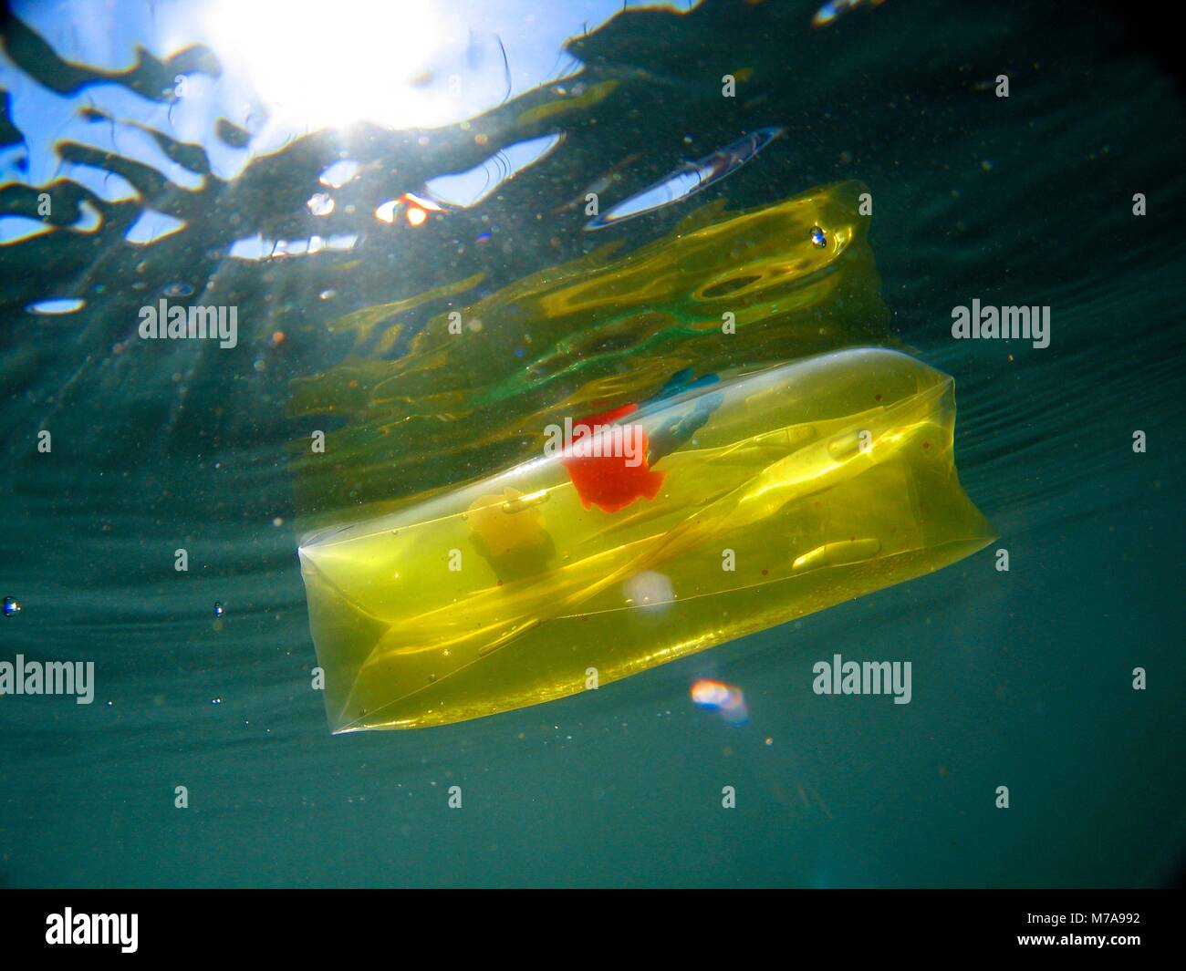 Yellow transparent children toy floating and causing water pollution. Aluminium foil floating and causing water pollution. Water pollution is largely  Stock Photo