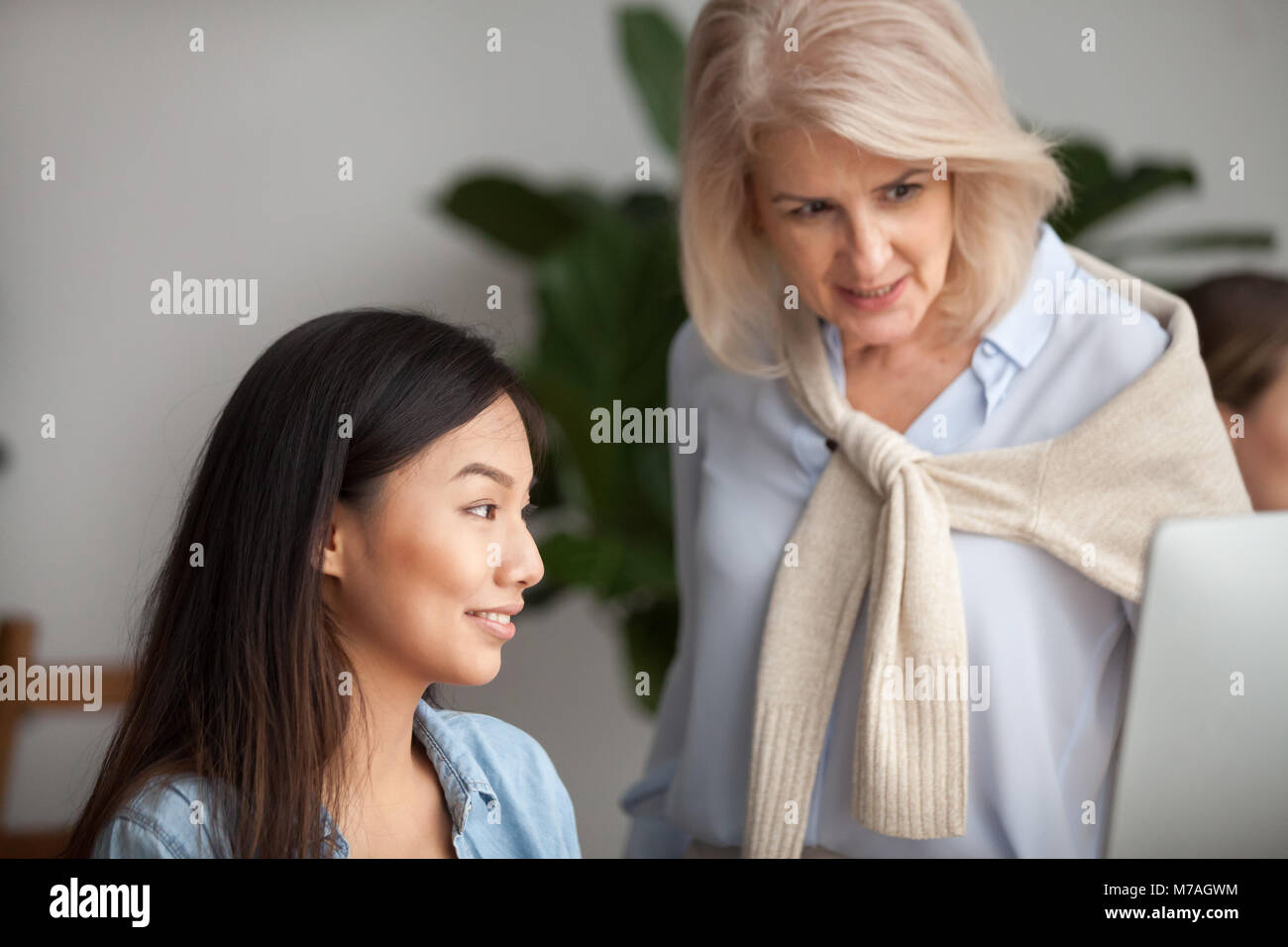 Smiling aged leader checking work or teaching young asian employ Stock Photo