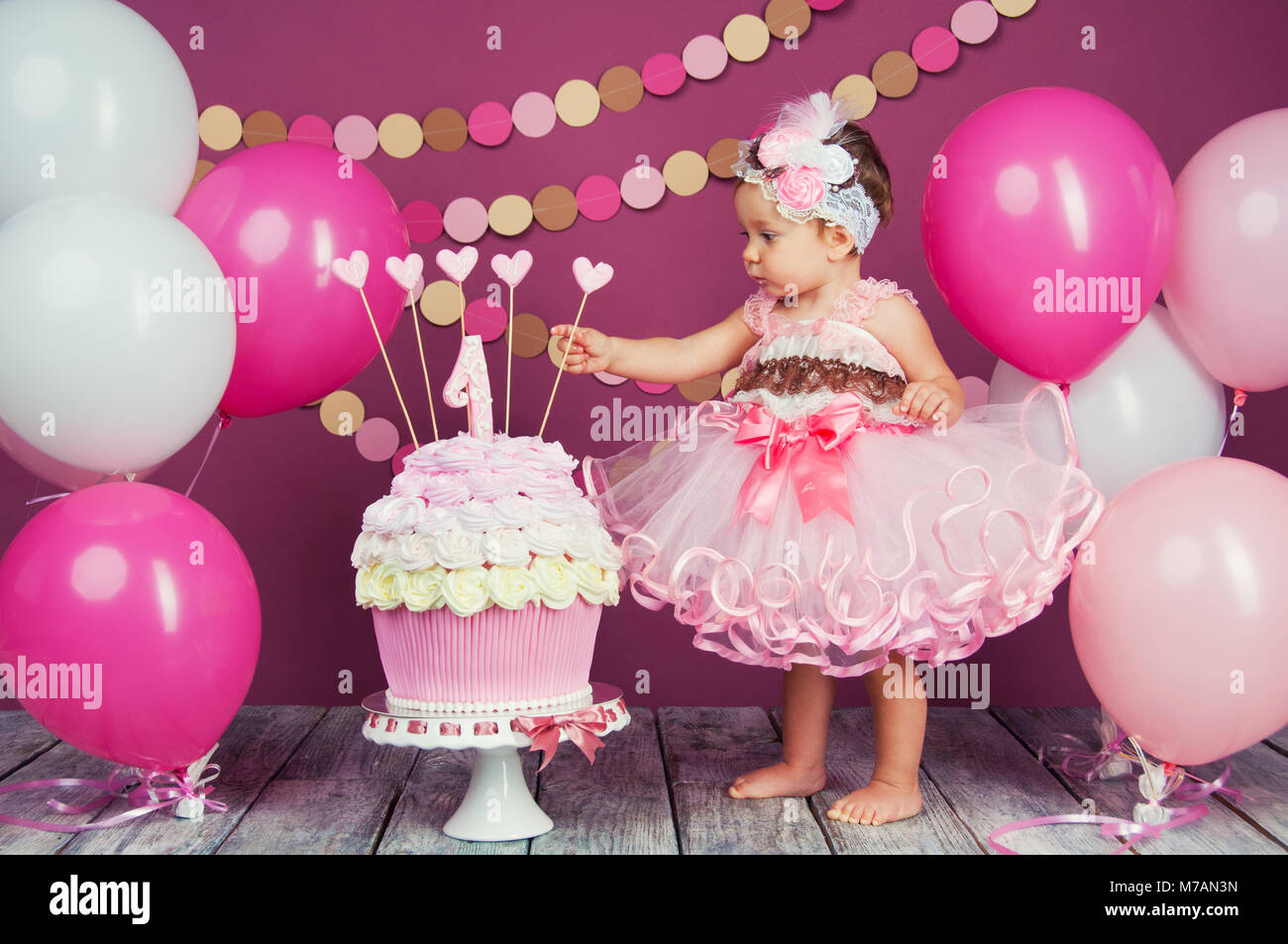 Portrait of a little cheerful birthday girl with the first cake. Eating